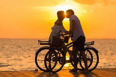Lune de miel Couple à vélo s'embrassant devant le coucher de soleil