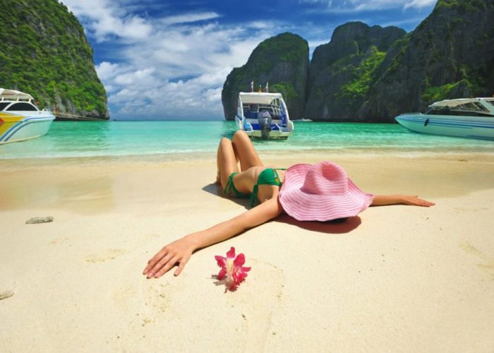 Femme alongée sur une plage de sable fin face à une eau turquoise