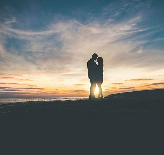 Couple enlacé au lever du soleil sur une plage